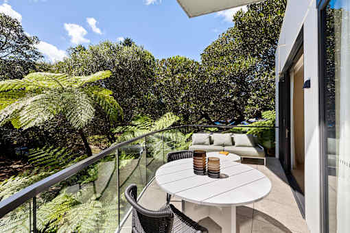 A balcony with a table and chairs overlooks a lush green garden.