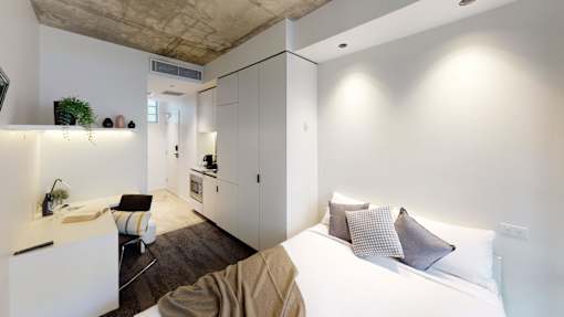 A modern bedroom with a bed, a chair, and a kitchen area.
