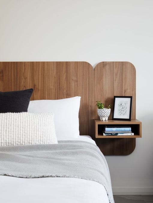 a bed with a wooden headboard and a nightstand with a plant and books