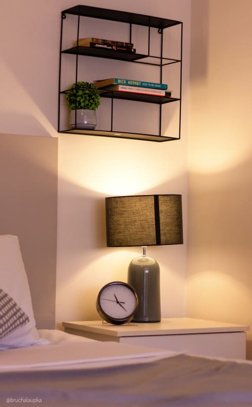 a nightstand with a clock and a lamp and a shelf with books