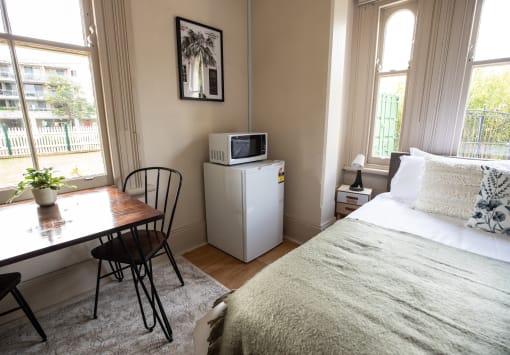 a bedroom with a bed and a desk and a microwave on a refrigerator