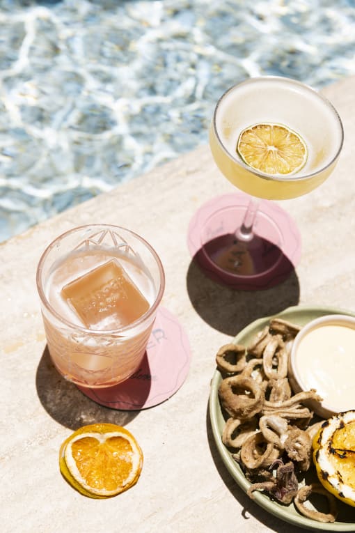 a cocktail and two glasses on a table next to a pool
