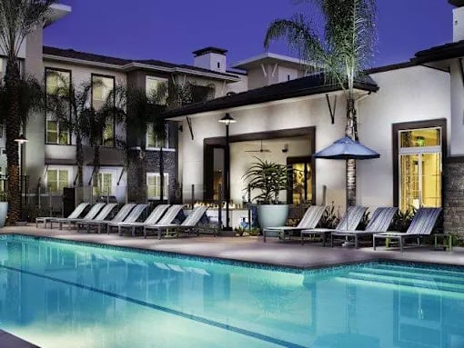 a hotel pool with lounge chairs and umbrellas at night