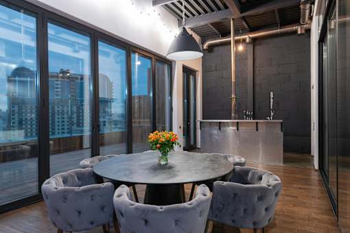 A round table with grey chairs and a vase of flowers in the middle.