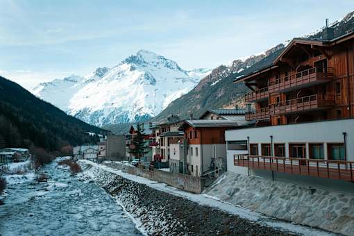 A river flows through a small town with snow-capped mountains in the background.