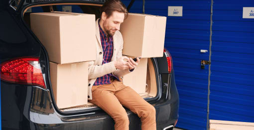 a man sitting in the trunk of a car with boxes on his phone