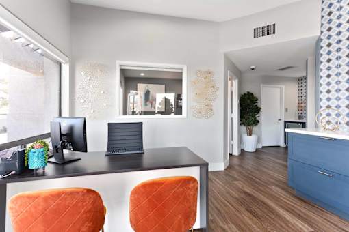 A modern office with a black desk and orange chairs.