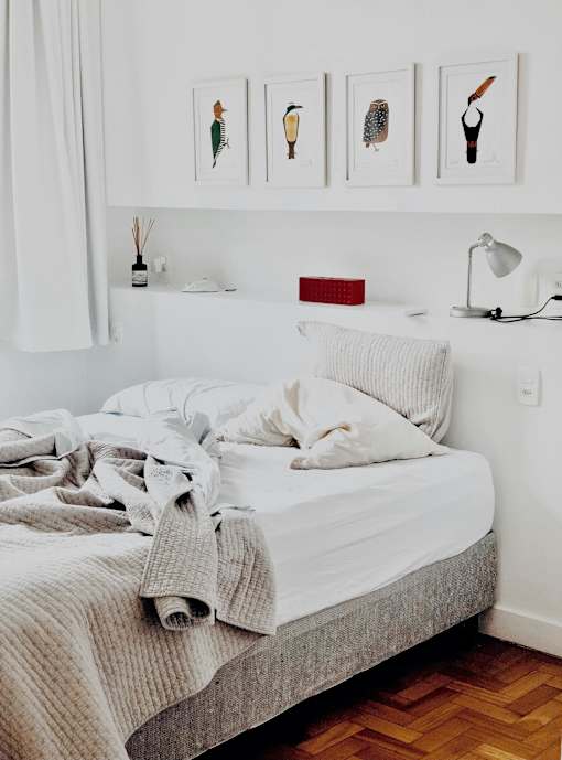 a bedroom with a bed with white sheets and pillows and a wall with pictures