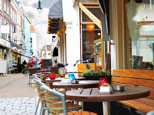 A street view of a cafe with tables and chairs outside.