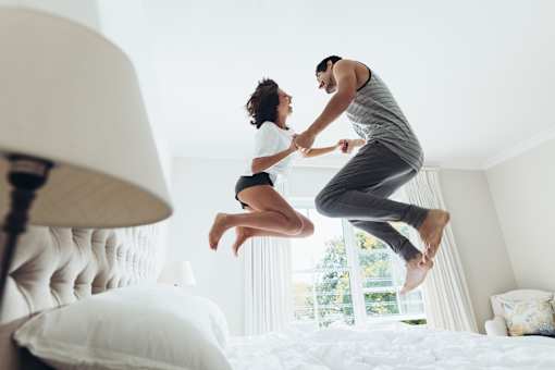 two people jumping on a bed in a hotel room