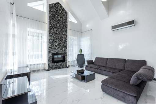 A grey couch sits in a white room with a stone pillar and a fireplace.