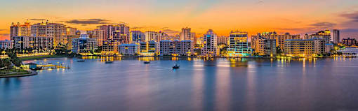 A city skyline at dusk with buildings reflecting on the water.