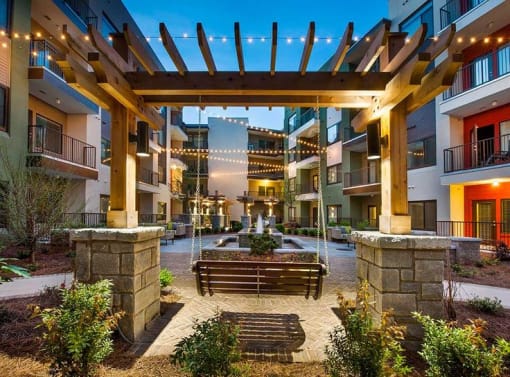 A wooden pergola is over a bench in a courtyard.