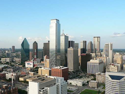A cityscape with a variety of buildings, including a tall skyscraper with a pointed top.