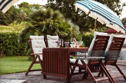 A wooden table with chairs and an umbrella is set up in a garden.