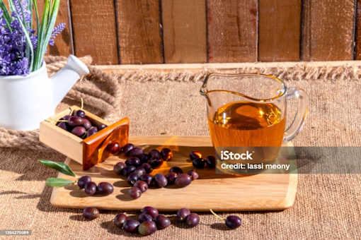 A glass pitcher of honey and a wooden tray with grapes on a burlap cloth.