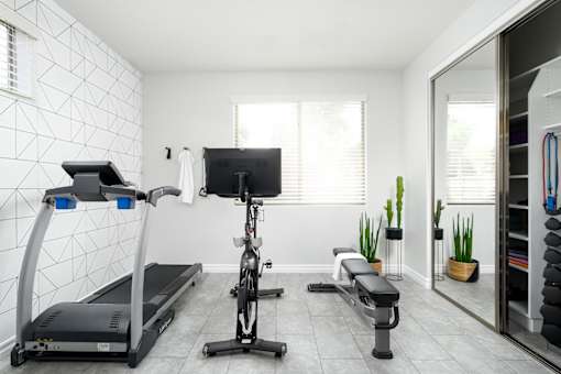 A well-equipped home gym with a treadmill, exercise bike, and bench.