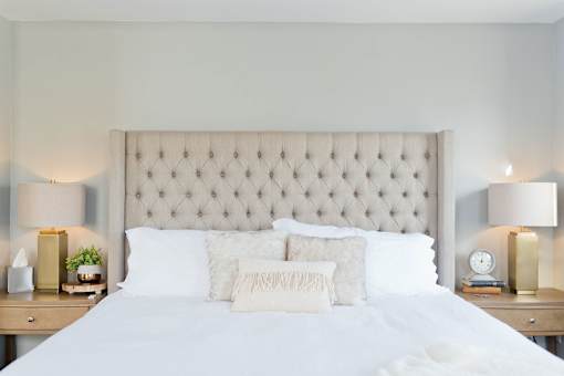 a bedroom with white bedding and a tan tufted headboard
