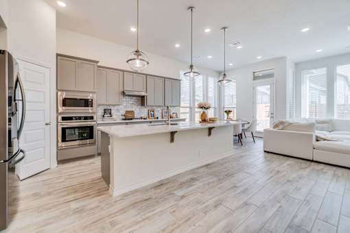 A modern clubhouse kitchen with a refrigerator on the left and a dining area with a table and chairs.