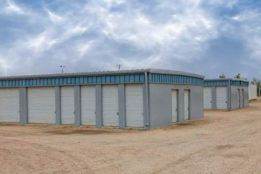 A large grey building with multiple roll-up doors is situated in a barren landscape.