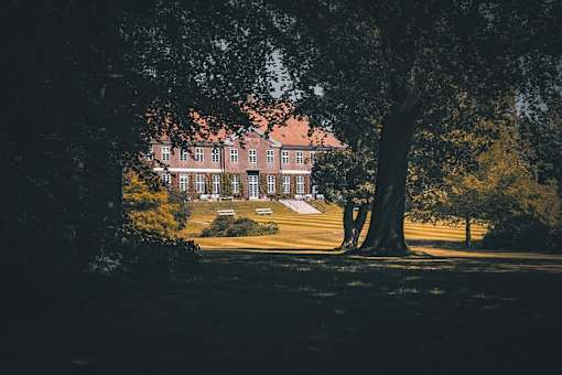 A large house is seen through the trees in the distance.