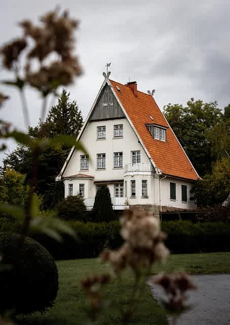A white house with a red roof is surrounded by greenery.