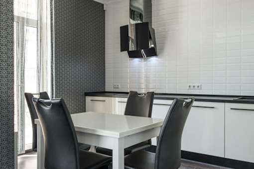 A white dining table with two black chairs in a modern kitchen.