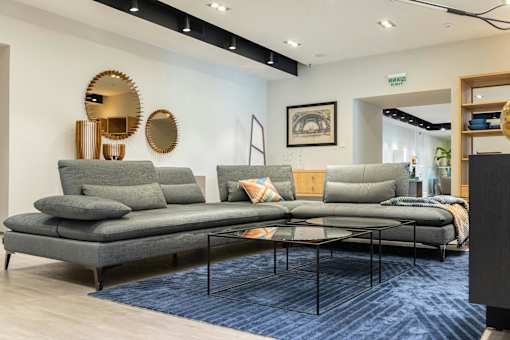 A living room with a grey sofa and a round mirror on the wall.