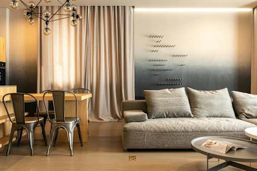 A modern living room with a grey couch, a wooden table, and a metal chair.