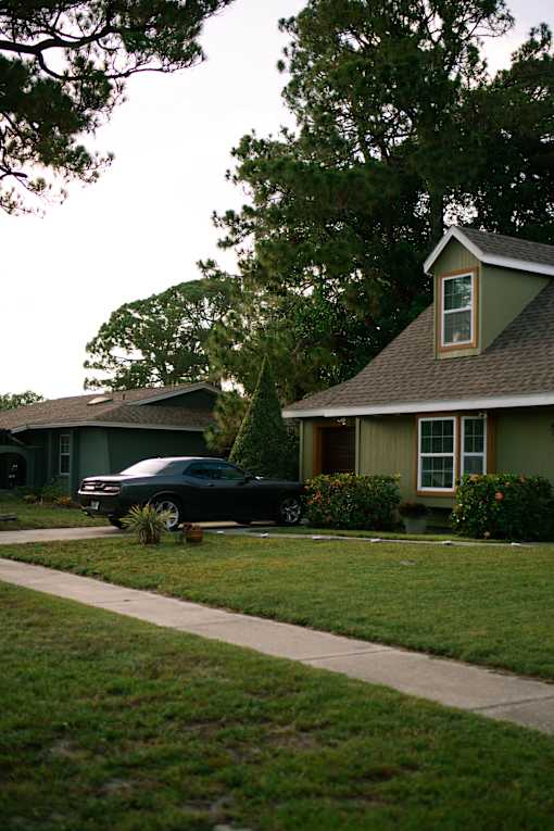 A black car is parked in front of a green house.