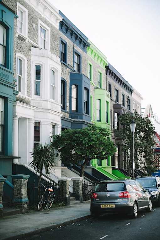 A street with cars parked on the side and a green tree in front of a building.