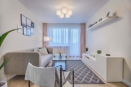 A living room with a grey couch, a black chair, a glass coffee table, and a white cabinet.