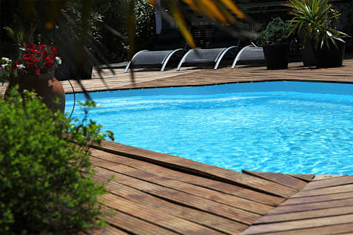A pool surrounded by wooden decking and lounge chairs.