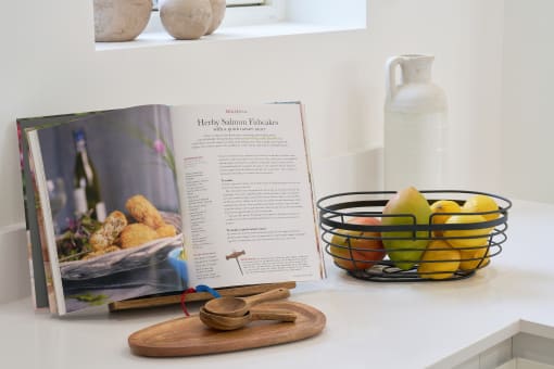 a cookbook sits on a counter next to a bowl of fruit