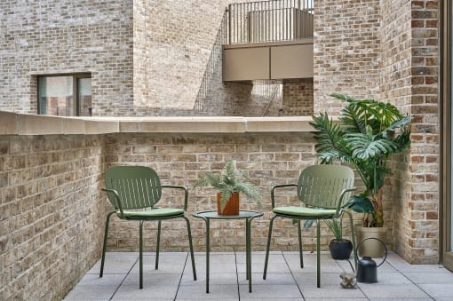 a patio with two green chairs and a small table with a plant on it