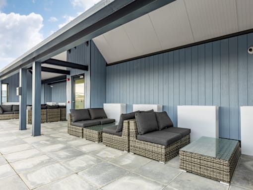 A patio with a wicker sofa and a glass table.