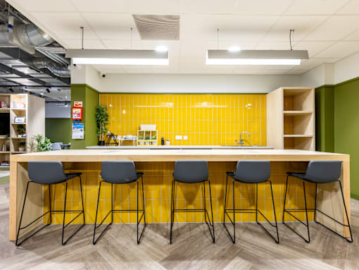 A yellow tiled wall behind a bar with four stools.