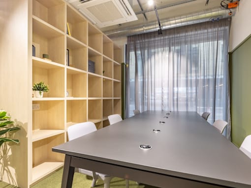 A conference room with a long table and chairs, a shelving unit, and a plant.