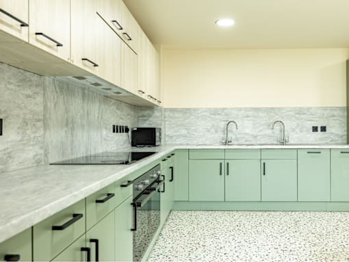 A kitchen with green cabinets and a marble backsplash.