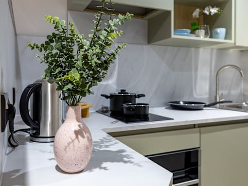 A pink vase with a green plant sits on a white countertop.