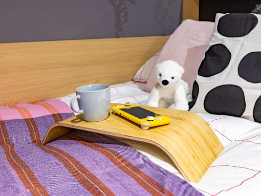 A teddy bear sits on a bed with a yellow toy car and a mug.