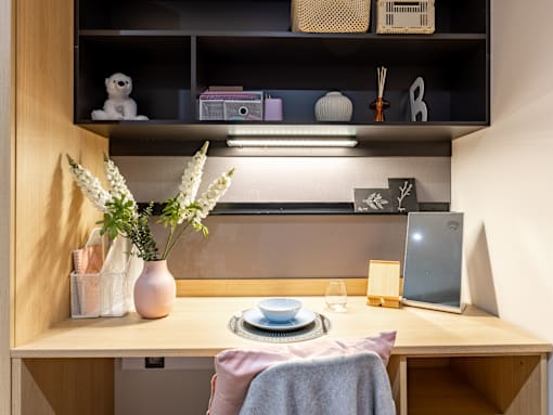 A desk with a laptop, a vase with flowers, and a small table with a plate and a cup.
