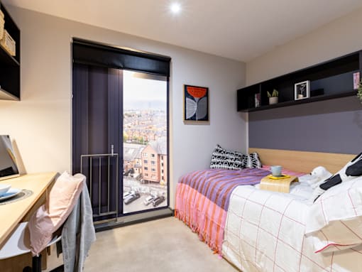 A bedroom with a bed, desk, and a window with a view of a city.