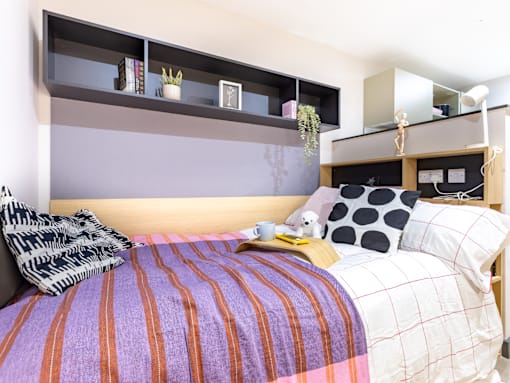 A bed with a striped purple and orange comforter and a black and white pillow.