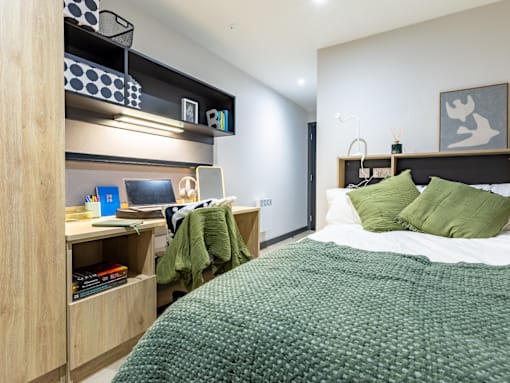 A bedroom with a bed, a desk with a laptop, and a bookshelf.