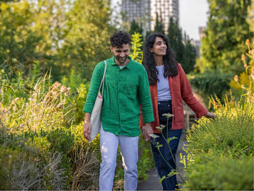 Two people walking through a green, leafy area.