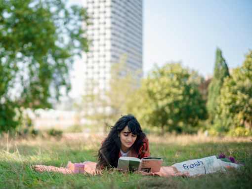 A woman is reading a book on a blanket in a grassy field.