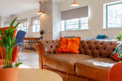 A brown leather couch with orange pillows sits in a living room.