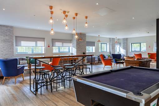 A pool table is in the middle of a room with a bar and chairs.