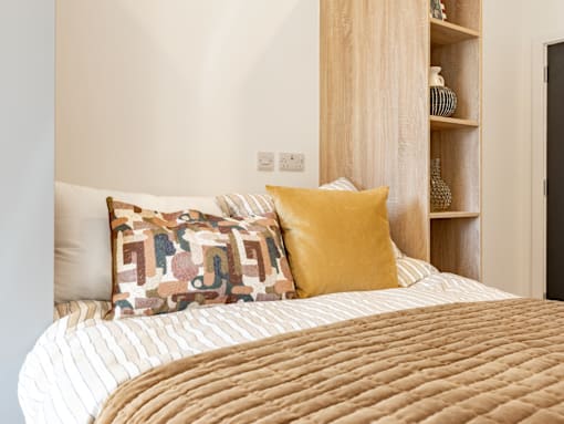 A bed with a white and tan comforter and two pillows with geometric patterns.